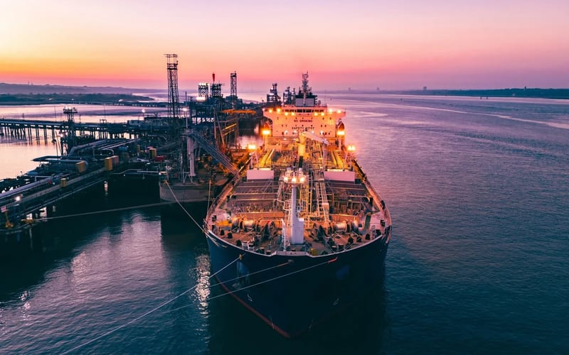 Oil tanker ship at port terminal with storage tanks at sunset